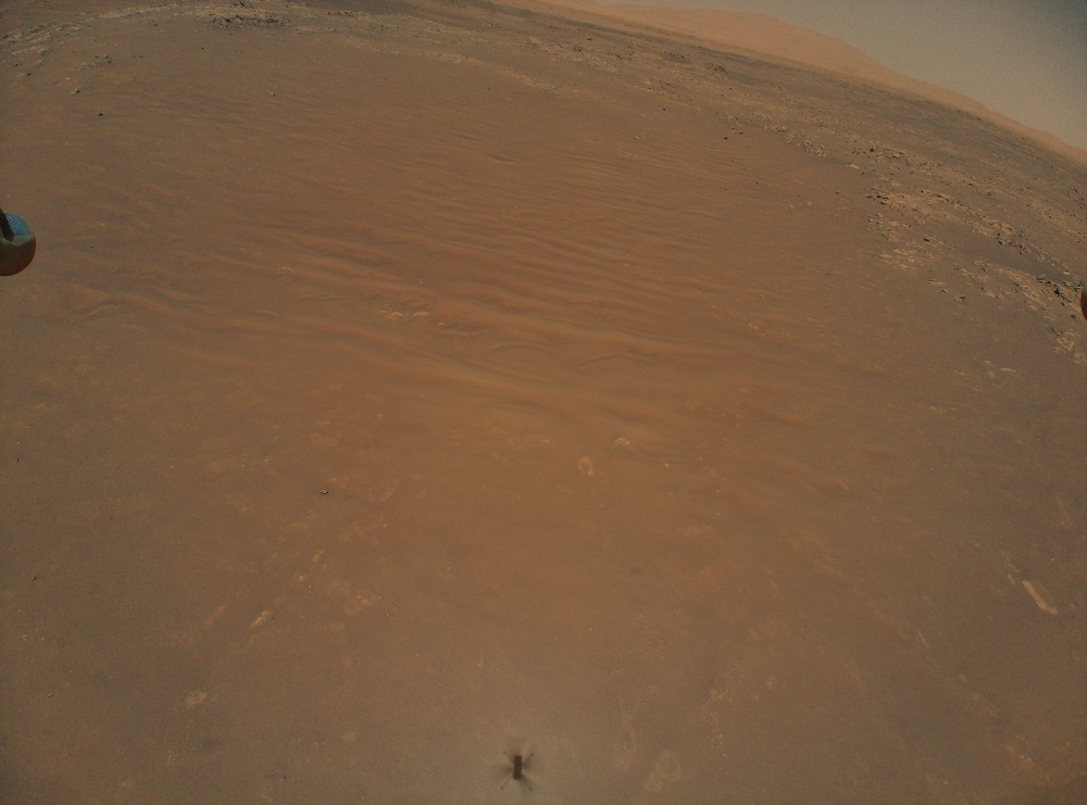 The image shows an aerial photograph of a creative helicopter recording the persevering rover on the surface of Mars