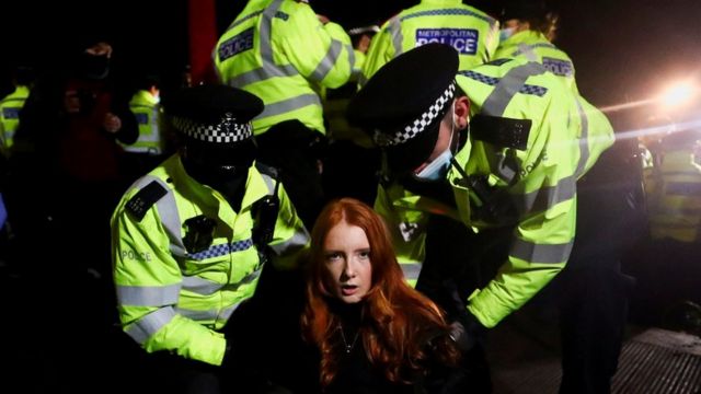A young woman with long hair is handcuffed by a number of unknown police officers