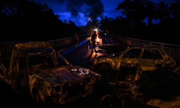 A man carries water bottles through a burning roadblock of burnt vehicles and rubble in the isolated village of La Buchen in Saint-Rose, on the French Caribbean island of Guadeloupe Photo: Christophe Arkampold / AFP