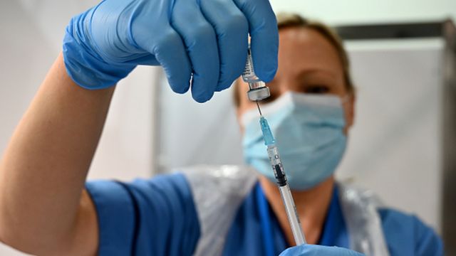 A health worker holds a syringe and ampoule with the vaccine