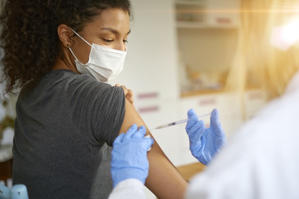 In the color image, a person is sitting while a person injects their arm.
