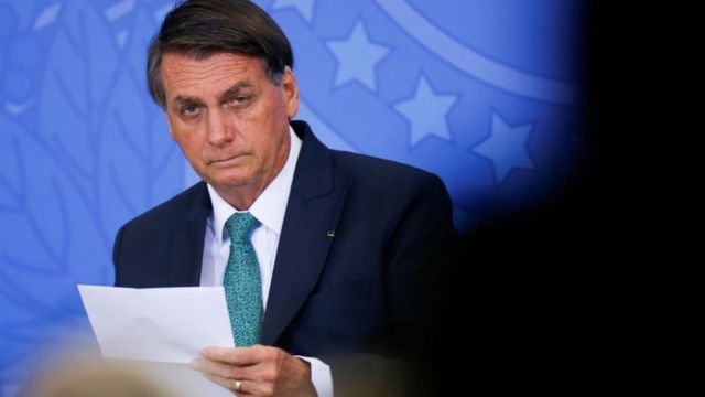 Bolsonaro sits at an event with a serious face looking forward