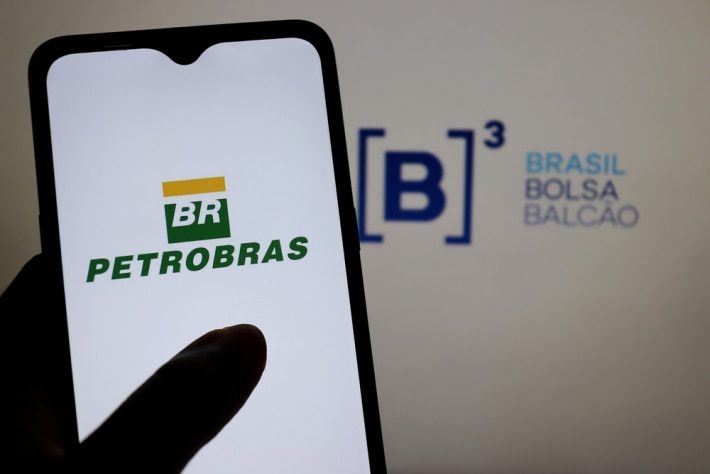 Hand holding smartphone with Petrobras logo.  In the background, the B3 . logo