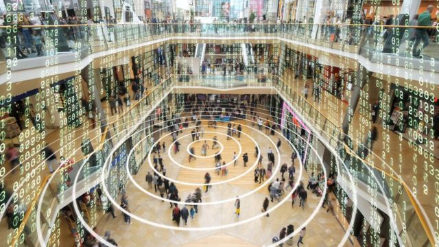 Color photography shows people in a mall and white matrix-type figures floating throughout the environment